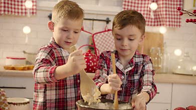 Cute boys making gingerbread dough together at the kitchen on Christmas eve