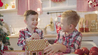 Cute boys decorating gingerbread house with topping and icing at the kitchen