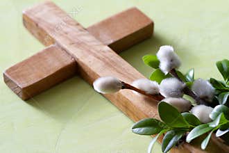 Wooden cross with boxwood twigs and catkins on green background. Palm Sunday concept