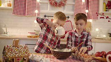 Cute boys making gingerbread dough together at the kitchen on Christmas eve