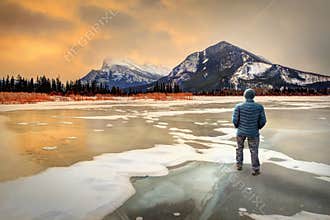 Man standing on frozen Vermilion Lakes in Banff watching golden sunrise over Mount Rundle