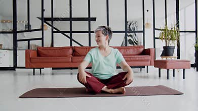 Old woman make yoga exercise at home. Mature woman have meditation. she sits down on the bed, looks out the window and