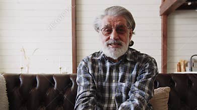 An elderly man in a plaid shirt makes a video call on a laptop. Satisfied old man looking at camera.