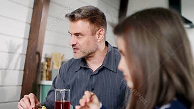 A family reunion concept. An adult father speaking to his wife at dining table. A small girl laughing when her daddy
