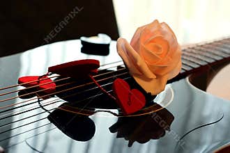 Pink rose and red hearts on the soundboard of a dark guitar.
