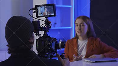 Backstage video production recording. A videographer uses a professional camera to film a female presenter sitting at a