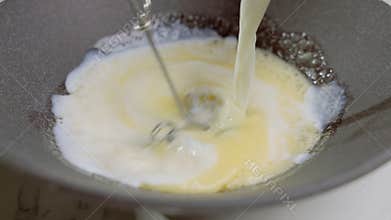The cook adds milk to beaten egg with sugar. Preparation of sweet food.