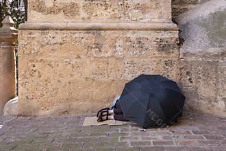 A homeless woman sleeps on the floor at the entrance to the cathedral in Malaga, Spain, covered by a black umbrella