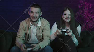 Funny young couple sitting on sofa at home and playing video games on console. Esport fans enjoying their