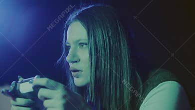 Young woman sitting on couch and playing portable console with neon light background. Playing games alone at home