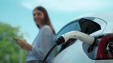 Woman using smartphone to pay for electric car charging. Exalt