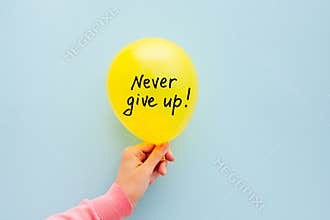 Never give up - lettering on yellow air balloon in woman hand, motivation phrase on light blue