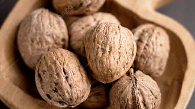 Ripe unshelled walnuts in shell in a shaped wooden craft bowl. Unpeeled raw nuts.