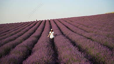 Girl is runs through a field of purple flowers. She is wearing a white shirt and a hat.