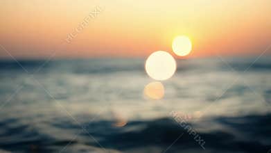 As the sun sets over the ocean the sparkling waves absorb its soft orange and pink hues creating a serene and dreamlike