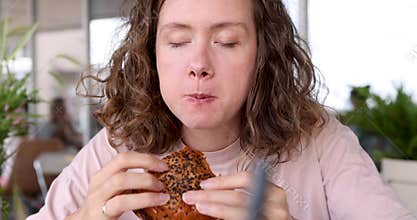 Woman is relishing delicious and savory burger while enjoying the cozy and relaxing cafe atmosphere