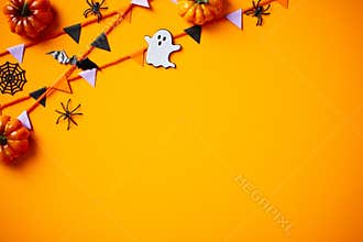 Halloween flat lay composition with pumpkins, spiders, ghosts, bunting flag garland on orange background. Flat lay, top view, copy