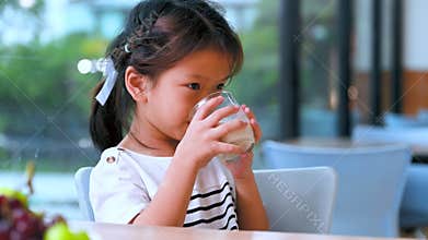 Asian kid girl sitting drinking plant-based milk in a clear glass, Happy child allergic to cow\'s milk.