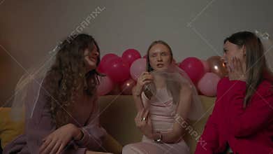 Group of young women friends and bride celebrating bachelorette party at home, bridesmaids sit on sofa and wait for
