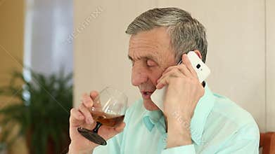 Man with cell phone sits at the table and drinks brandy