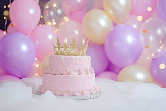 Pink princess birthday cake with golden crown and pastel balloons