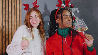 Two joyful women in festive reindeer antlers celebrate with sparkling drinks in front of a beautifully decorated