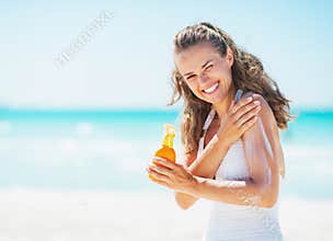 Smiling young woman applying sun block creme on beach