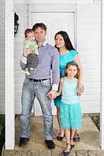 Father, mother, baby and daughter stand on porch of house.