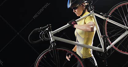 Young Caucasian woman cyclist carries her bicycle on her shoulder on a black background