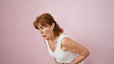 Suffering middle age lady in a dress, visibly ill, painfully clutching her aching stomach while standing, isolated over a pink