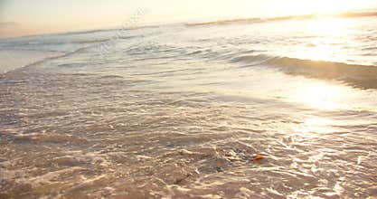 Gentle waves wash over the sandy shore at sunset, with a warm glow on the horizon, with copy space