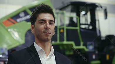 Young handsome tractor salesman is standing on the wrong side of large transport.