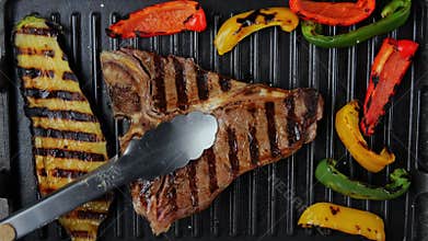 T- bone beef steak turn over on grill, with grilled vegetables. Slow motion. Top view