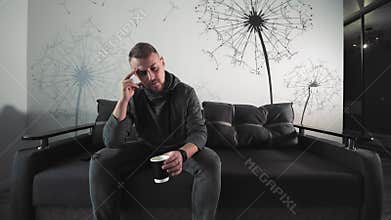 Man with Headache Holding Coffee, Man in thoughtful pose with coffee, experiencing a headache or stress, seated on a
