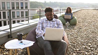 Business man sitting at chair bag on roof top outdoors and typing on laptop.