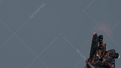 An ignited gelatin or agar pill of white and turquoise color, isolated on a grey background, burns, melts, foams, chars