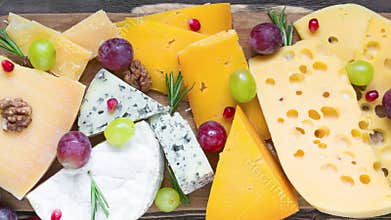 Assortment cheeses on wooden cutting board. Cheese plate served with grape fruits, tomatoes and rosemary, various cheese