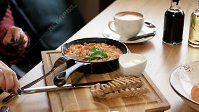 Woman eating beaten eggs with tomatoes for breakfast and drinking coffee. Breakfast at the restaurant
