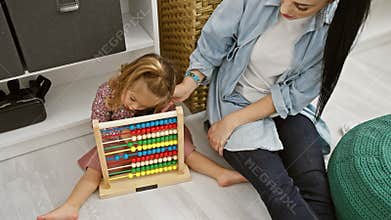 A woman in a denim shirt helps a young girl with an abacus in a contemporary room setting