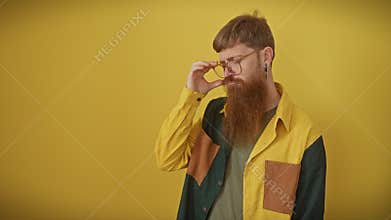 Stressed young redhead man, tired eyes behind glasses rubbing aching nose standing in frustration. headache pressure, fatigue