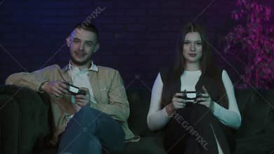 Funny young couple sitting on sofa at home and playing video games on console. Esport fans enjoying their playstation