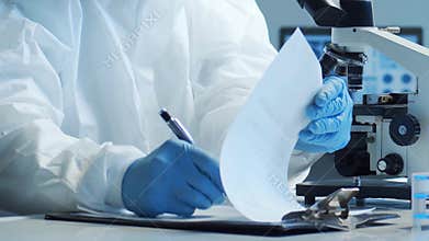 Scientist in protection suit and masks working in research lab using laboratory equipment: microscopes, test tubes