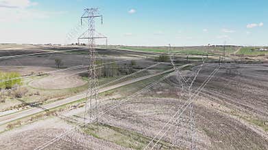 Aerial electrical towers above power lines cinematic shot overlooking seeded agriculture fields in Alberta Canada.