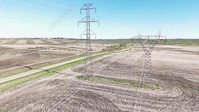 Between power lines cinematic shot overlooking steel lattice electrical pylons and prairie fields.