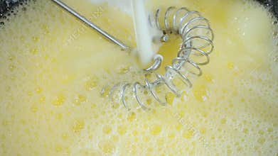 Adding milk to beaten egg with sugar to make a thin pancake batter.