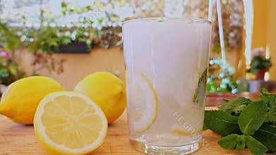 Liquid with gas is poured into a glass with ice, lemon and mint. Slow motion. Outdoors