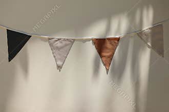 Vintage style orange, black, white textile bunting flags against beige wall background in sunlight. Simple fabric