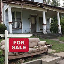 House For Sale Real Estate Sign in front of a Shabby Fixer Upper Home.