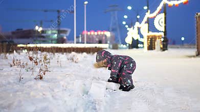 A child in a colorful snowsuit builds with snow blocks