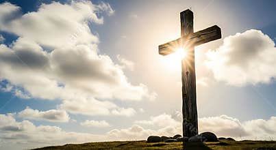 Wooden cross on a hill with sun and clouds in the background